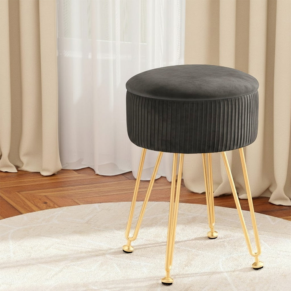 Gray cushioned stool with gold legs on a rug in front of curtains